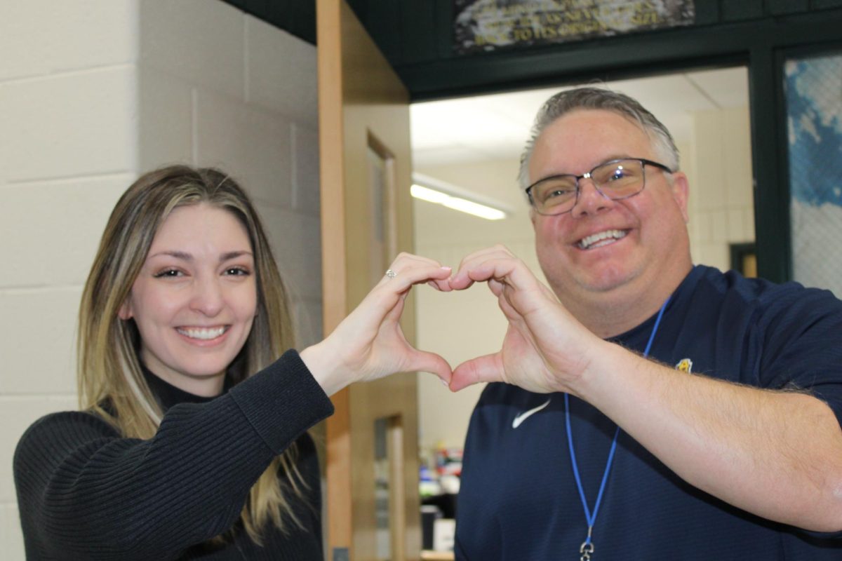 History teachers Mrs. Brockman and Mr. VanOrman make a heart with their hands. 