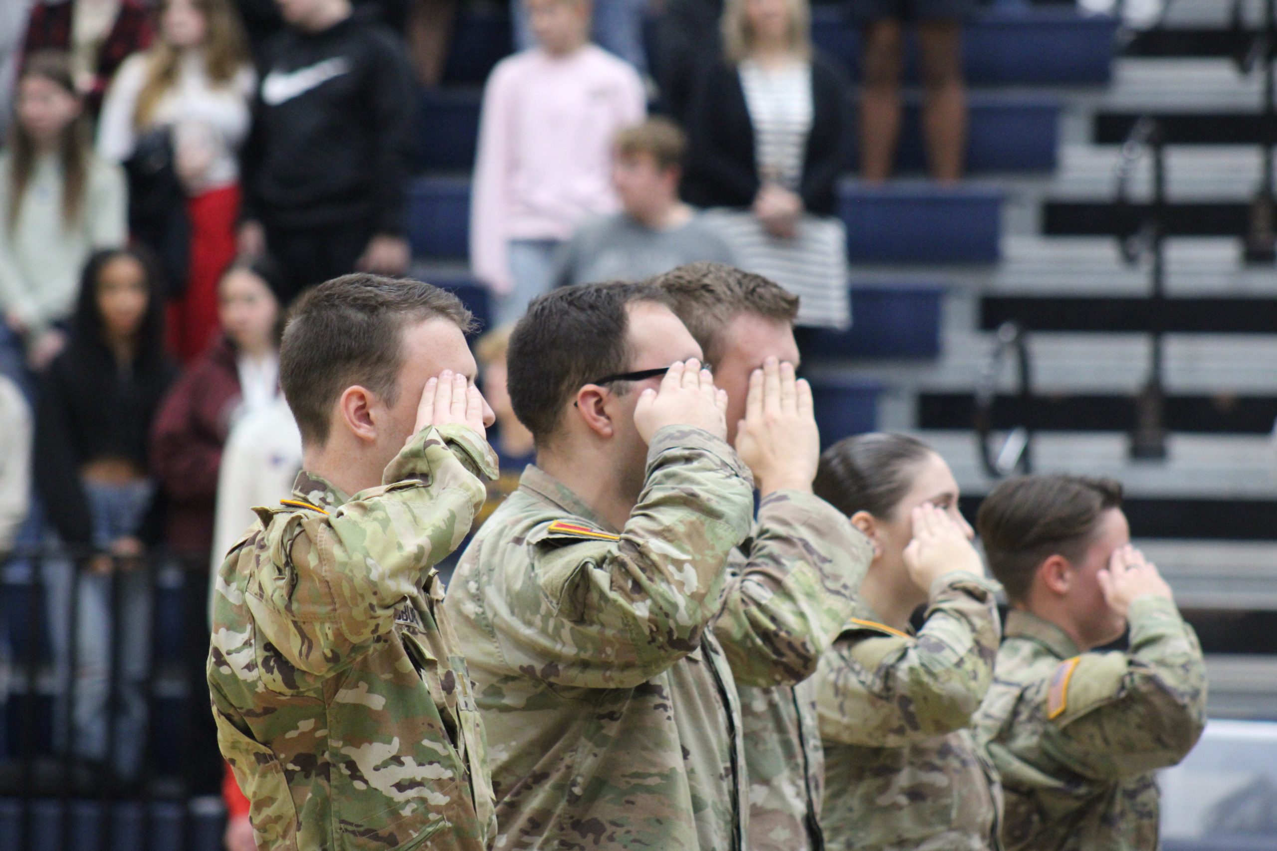 Active duty service members saluting the flag at MPHS's Veterans day Assembly 